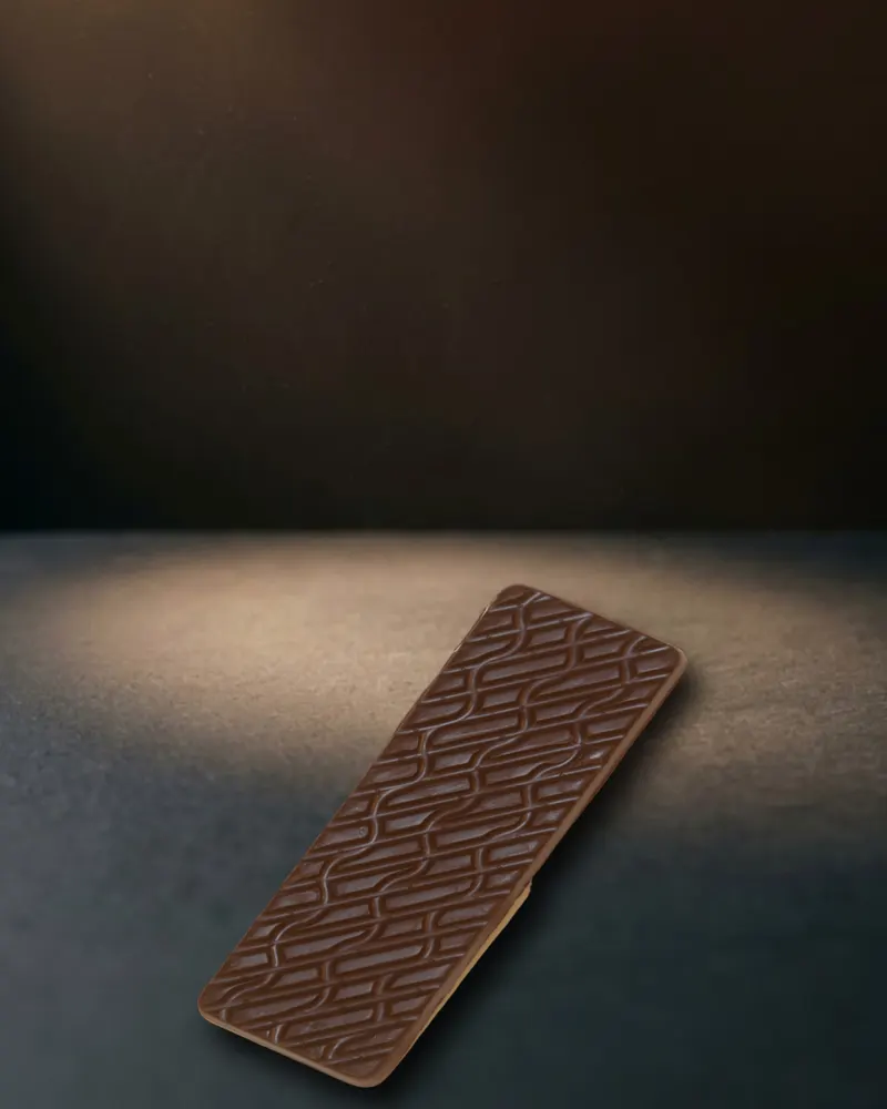 A dark chocolate bar with an interlocking ridge pattern, lying in a pool of warm light on dark slate